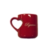 A red ceramic coffee mug with the word Ryerson in white cursive text appearing on the side in the shape of a heart along with a handle in the shape of a heart